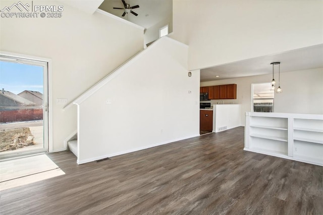 unfurnished living room with dark wood-style flooring, visible vents, a towering ceiling, baseboards, and stairway