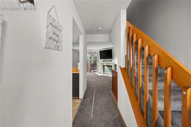 hallway with stairs, a textured wall, a textured ceiling, and light colored carpet