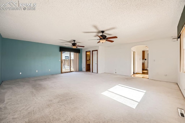 carpeted spare room featuring a ceiling fan, arched walkways, and a textured ceiling