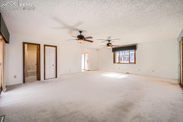 carpeted spare room with ceiling fan, arched walkways, and a textured ceiling