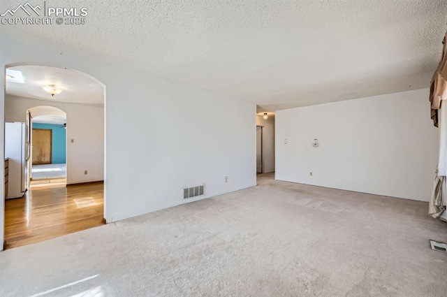 unfurnished room with visible vents, arched walkways, a textured ceiling, and light colored carpet