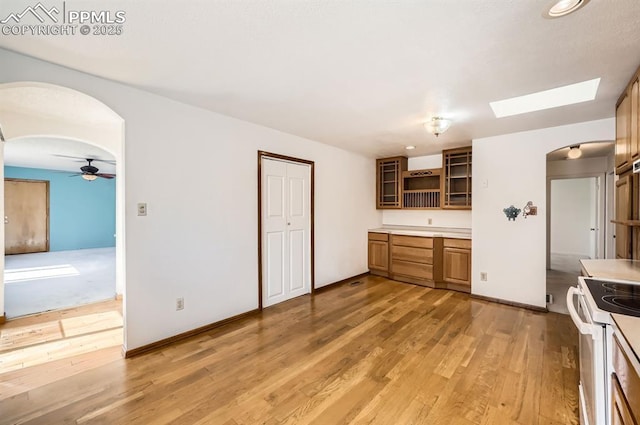 kitchen with arched walkways, white electric stove, open shelves, light wood-style flooring, and glass insert cabinets