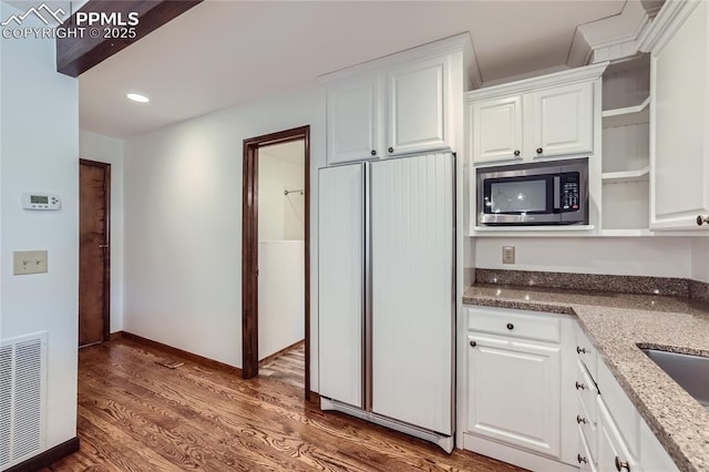 kitchen with wood finished floors, white cabinets, fridge, open shelves, and stainless steel microwave