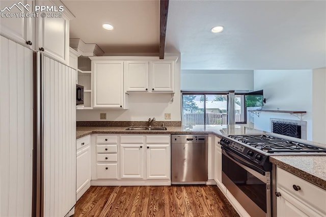 kitchen featuring built in appliances, a fireplace, wood finished floors, a sink, and white cabinets