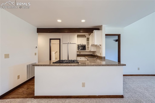 kitchen with built in appliances, a sink, visible vents, white cabinetry, and dark stone countertops