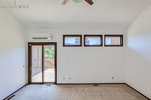 carpeted empty room with a wall unit AC, baseboards, visible vents, and a textured ceiling