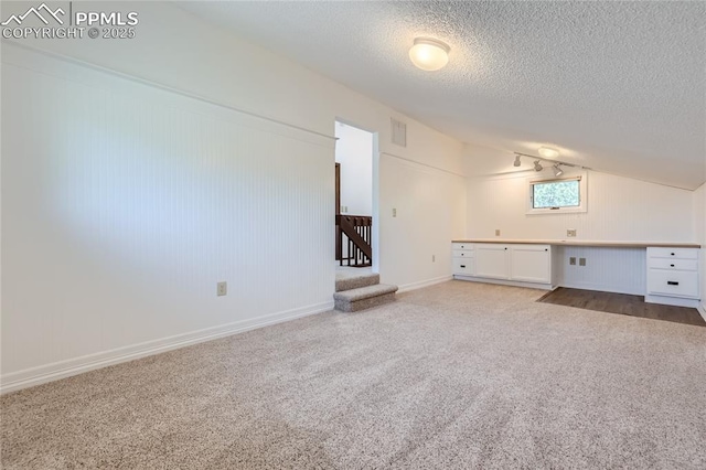 additional living space featuring visible vents, built in study area, carpet, vaulted ceiling, and a textured ceiling