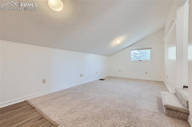 bonus room with lofted ceiling, visible vents, a textured ceiling, baseboards, and stairs