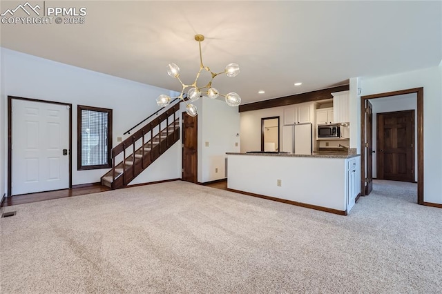 unfurnished living room featuring carpet flooring, a notable chandelier, baseboards, and stairs