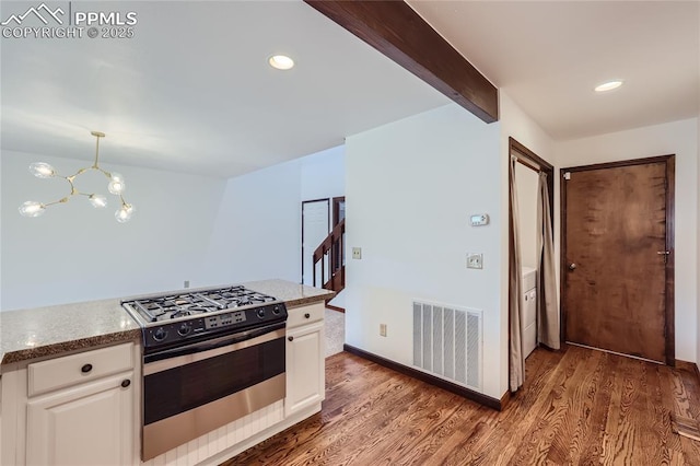 kitchen featuring beam ceiling, gas stove, wood finished floors, and visible vents