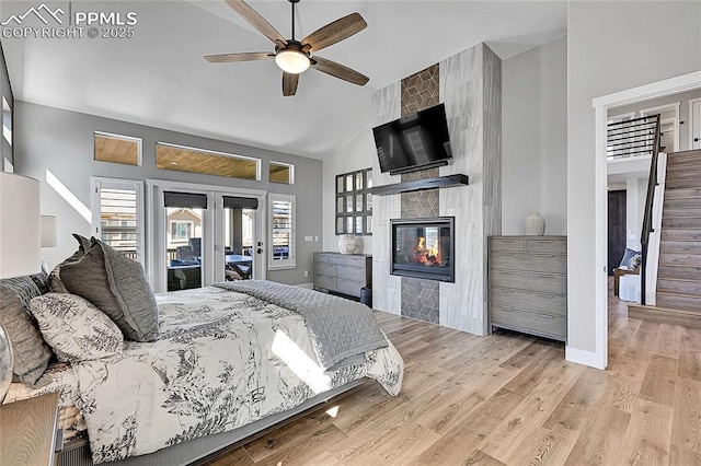 bedroom with a large fireplace, baseboards, wood finished floors, access to outside, and high vaulted ceiling