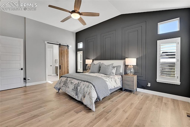 bedroom featuring light wood-style floors, lofted ceiling, baseboards, and a barn door