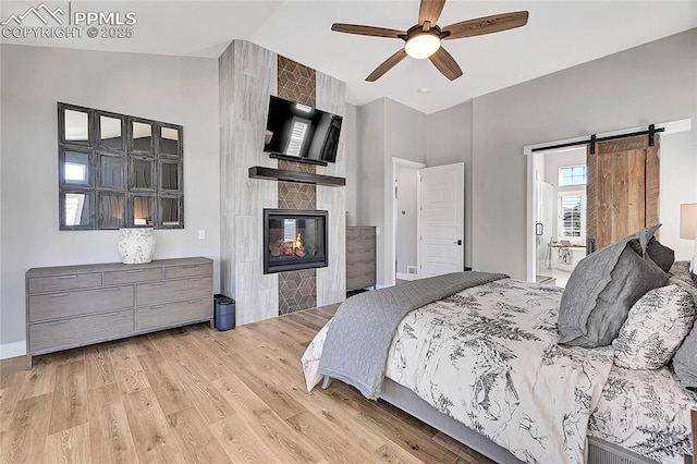 bedroom with light wood-style floors, a barn door, a fireplace, and high vaulted ceiling