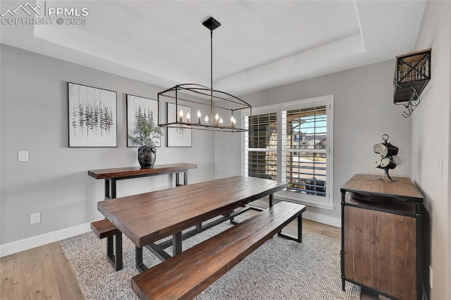 dining room with a notable chandelier, a tray ceiling, light wood-type flooring, and baseboards