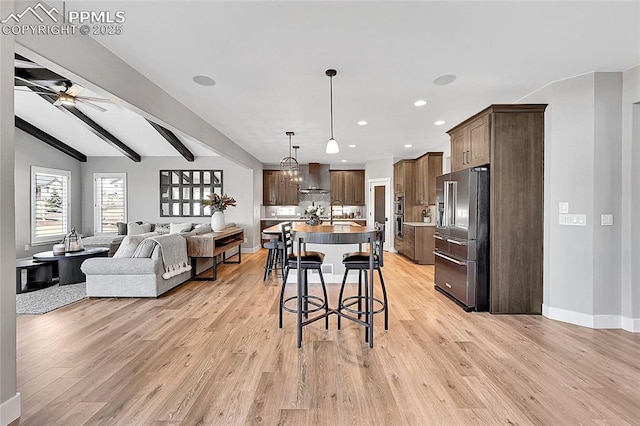 kitchen featuring light wood-style flooring, ceiling fan, open floor plan, stainless steel appliances, and wall chimney range hood