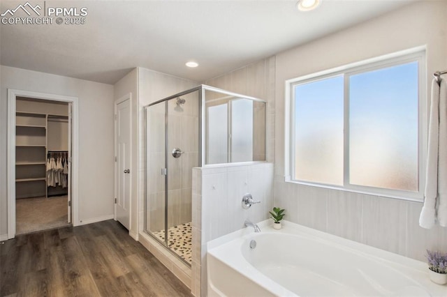 bathroom with a garden tub, recessed lighting, wood finished floors, a stall shower, and a walk in closet