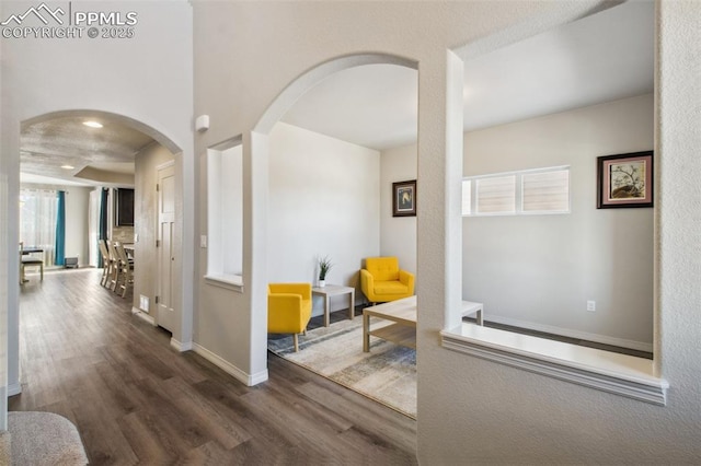 hall with dark wood-style floors, arched walkways, and baseboards