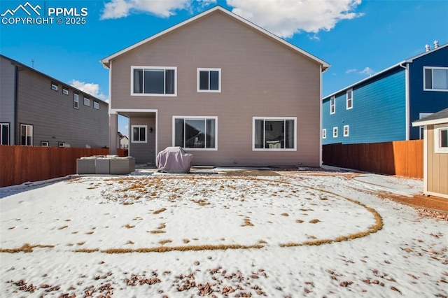 snow covered house featuring a hot tub, a fenced backyard, and a patio