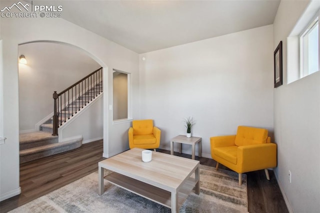 living area featuring stairs, arched walkways, baseboards, and wood finished floors