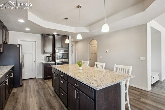 kitchen with arched walkways, a breakfast bar area, appliances with stainless steel finishes, a tray ceiling, and dark wood finished floors