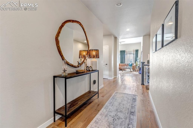 corridor with baseboards, a textured wall, and light wood finished floors