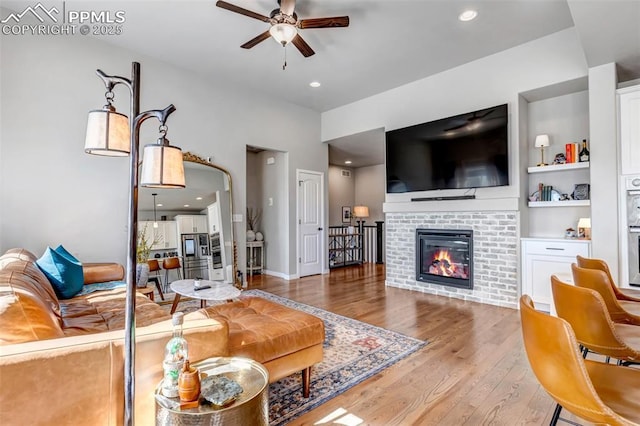 living area with built in shelves, a fireplace, recessed lighting, light wood-style flooring, and ceiling fan