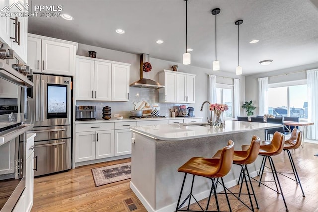 kitchen with a sink, visible vents, light wood-style floors, wall chimney range hood, and appliances with stainless steel finishes