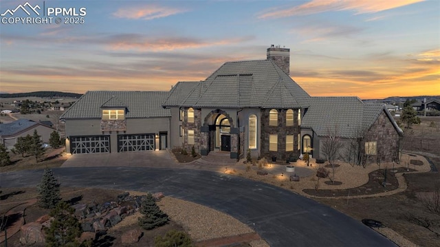 french country style house featuring driveway, stone siding, and a tile roof