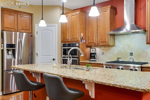 kitchen featuring brown cabinets, wall chimney range hood, stainless steel appliances, and decorative light fixtures