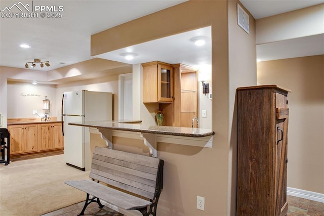 kitchen featuring a breakfast bar area, visible vents, glass insert cabinets, freestanding refrigerator, and light stone countertops