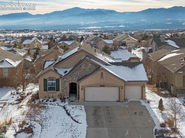 view of front facade featuring stucco siding, a mountain view, a garage, stone siding, and driveway