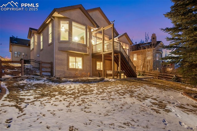 snow covered rear of property with a balcony, fence, stairway, and stucco siding