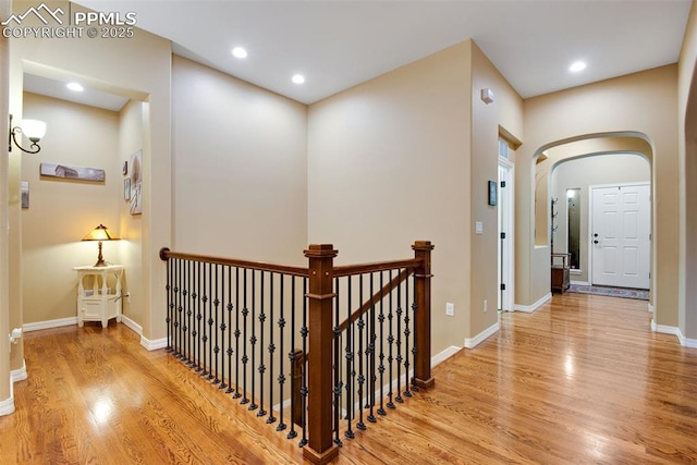 hallway with light wood finished floors, baseboards, arched walkways, an upstairs landing, and recessed lighting