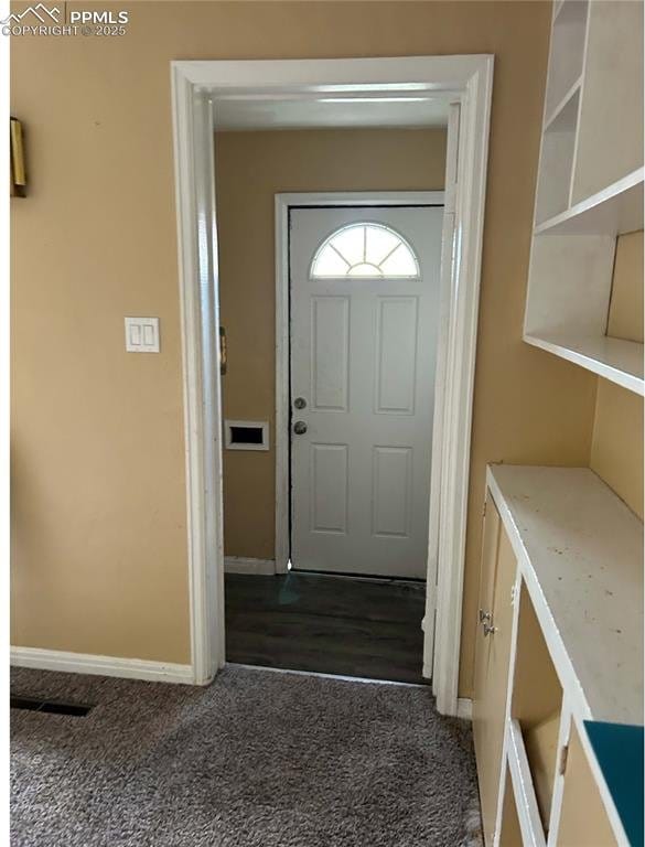 foyer entrance featuring baseboards and dark colored carpet