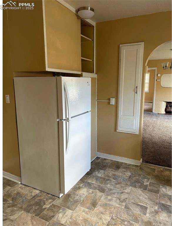 kitchen featuring arched walkways, freestanding refrigerator, and stone finish flooring