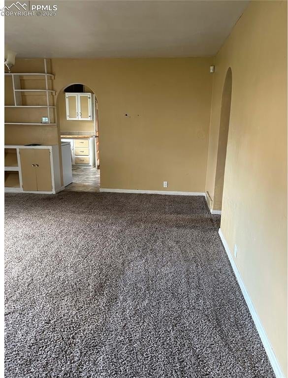 empty room featuring dark carpet, arched walkways, and baseboards