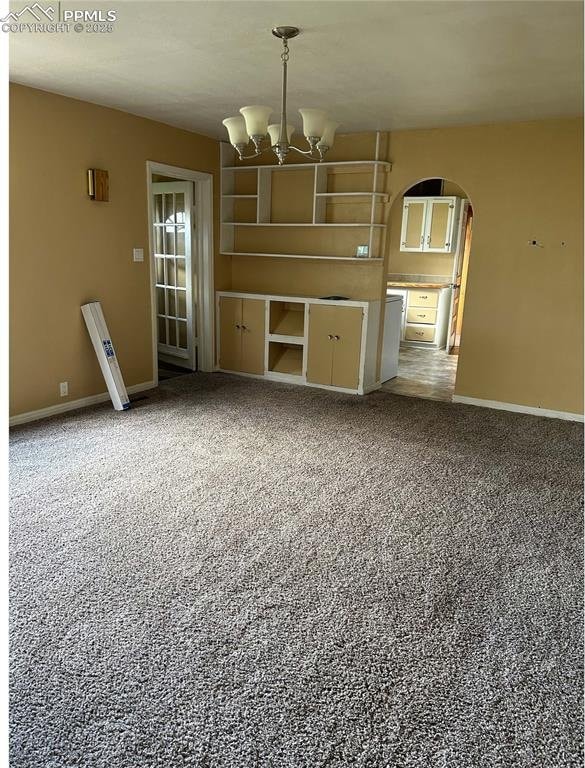 unfurnished living room with carpet, arched walkways, a notable chandelier, and baseboards