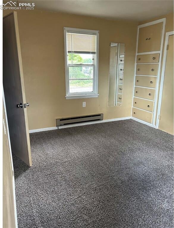 unfurnished room featuring a baseboard heating unit, baseboards, and carpet flooring