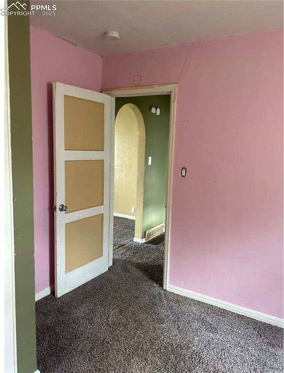 spare room featuring arched walkways, carpet flooring, visible vents, and baseboards