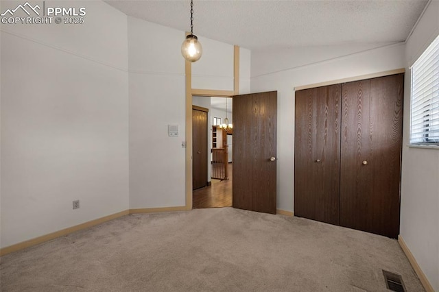 unfurnished bedroom with lofted ceiling, a chandelier, carpet flooring, visible vents, and baseboards