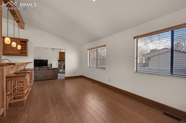 unfurnished living room featuring visible vents, baseboards, lofted ceiling, wood-type flooring, and a fireplace