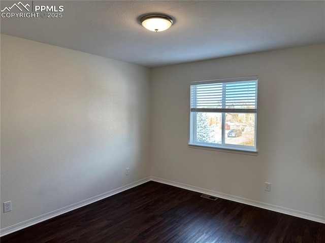 unfurnished room featuring dark wood-type flooring, visible vents, and baseboards