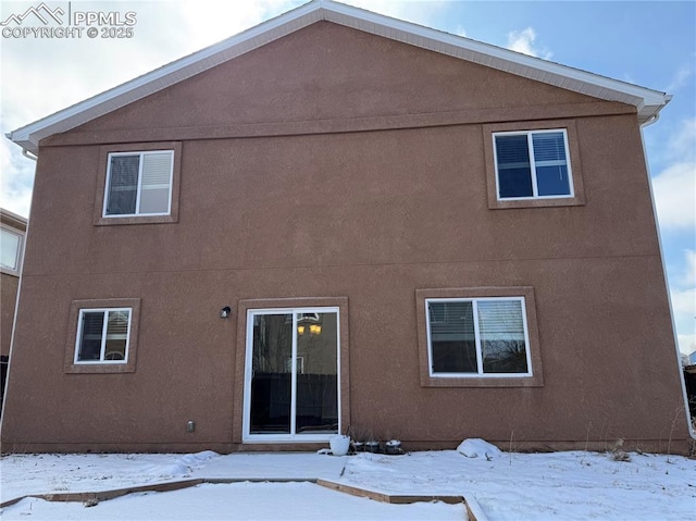 snow covered rear of property featuring stucco siding