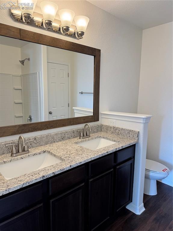 full bath with double vanity, a sink, toilet, and wood finished floors