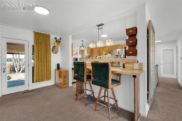 kitchen with light carpet, under cabinet range hood, a breakfast bar, and freestanding refrigerator