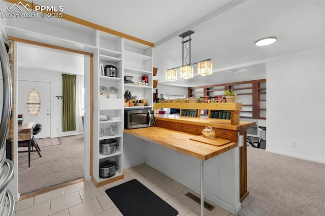 kitchen featuring butcher block counters, light colored carpet, stainless steel microwave, visible vents, and light tile patterned flooring