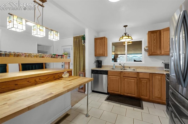 kitchen featuring stainless steel appliances, butcher block countertops, a sink, and decorative light fixtures