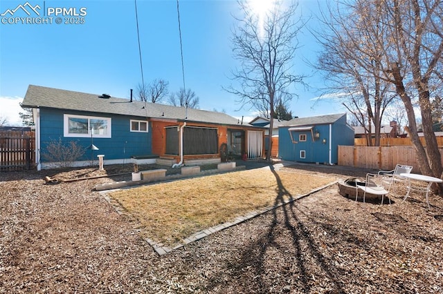 rear view of property featuring a fire pit, an outbuilding, and fence