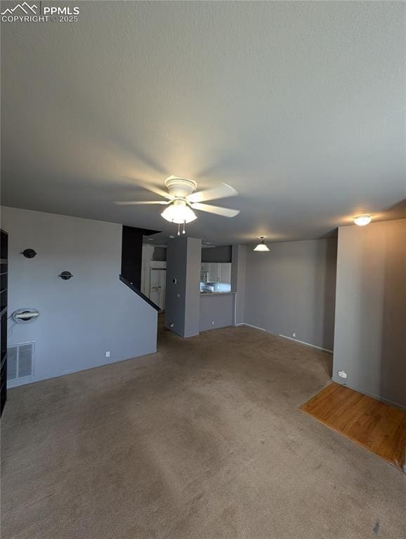 unfurnished living room featuring ceiling fan, carpet floors, a textured ceiling, and visible vents