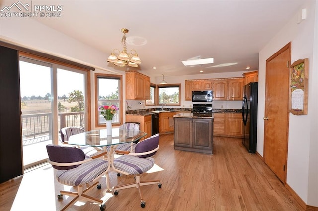 kitchen with light wood finished floors, dark countertops, a sink, a chandelier, and black appliances